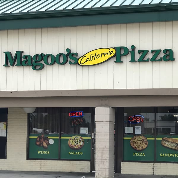 The exterior of Magoo's California Pizza, featuring its green and yellow sign and window decals of food.