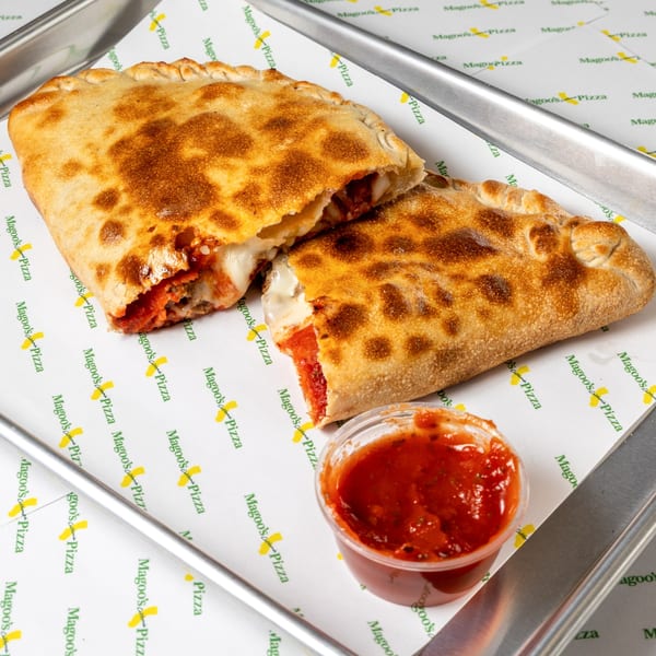 Two golden-brown Magoo's California Pizza calzones, one cut open, with a side of marinara sauce.