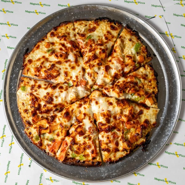 A Magoo's California Pizza, sliced and topped with melted cheese and chicken, on a metal pan.