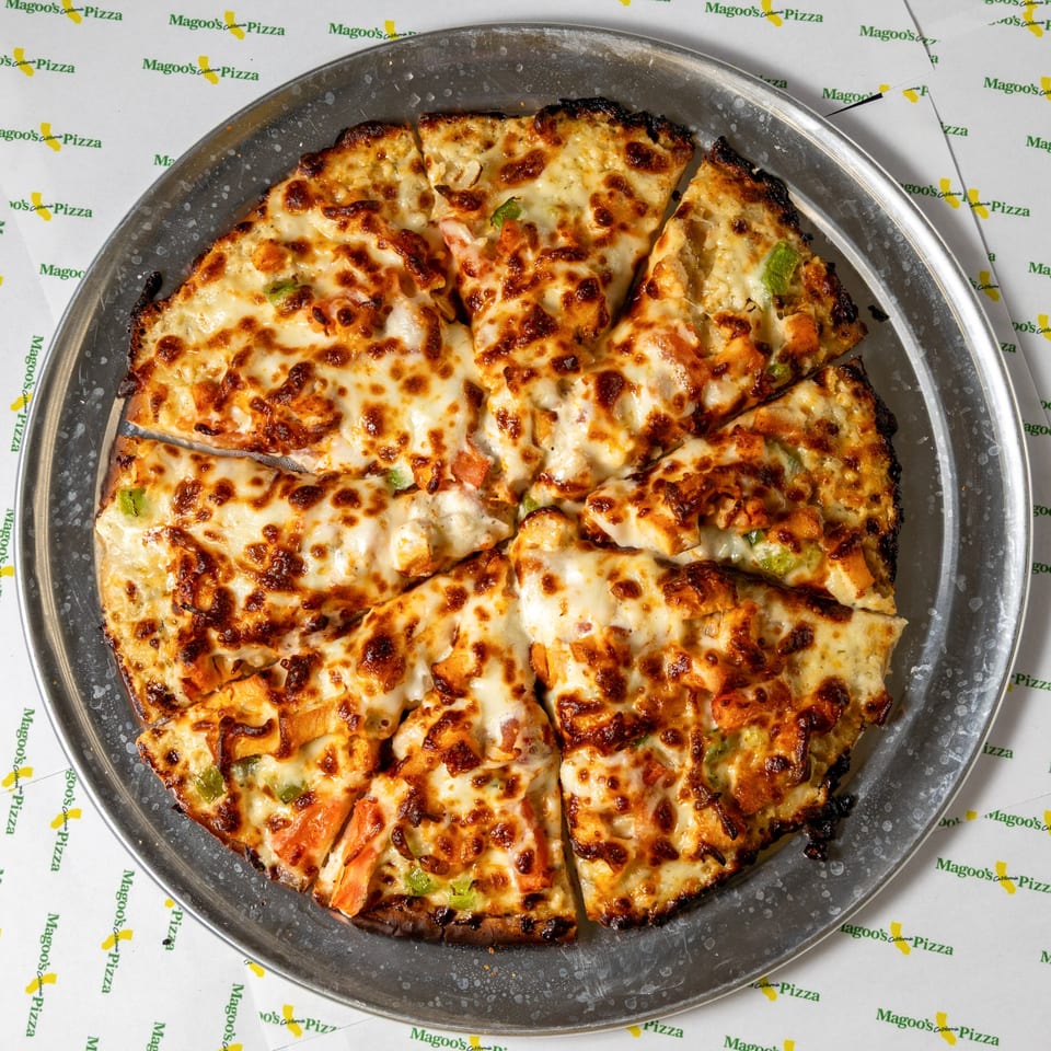 A Magoo's California Pizza, sliced and topped with melted cheese and chicken, on a metal pan.