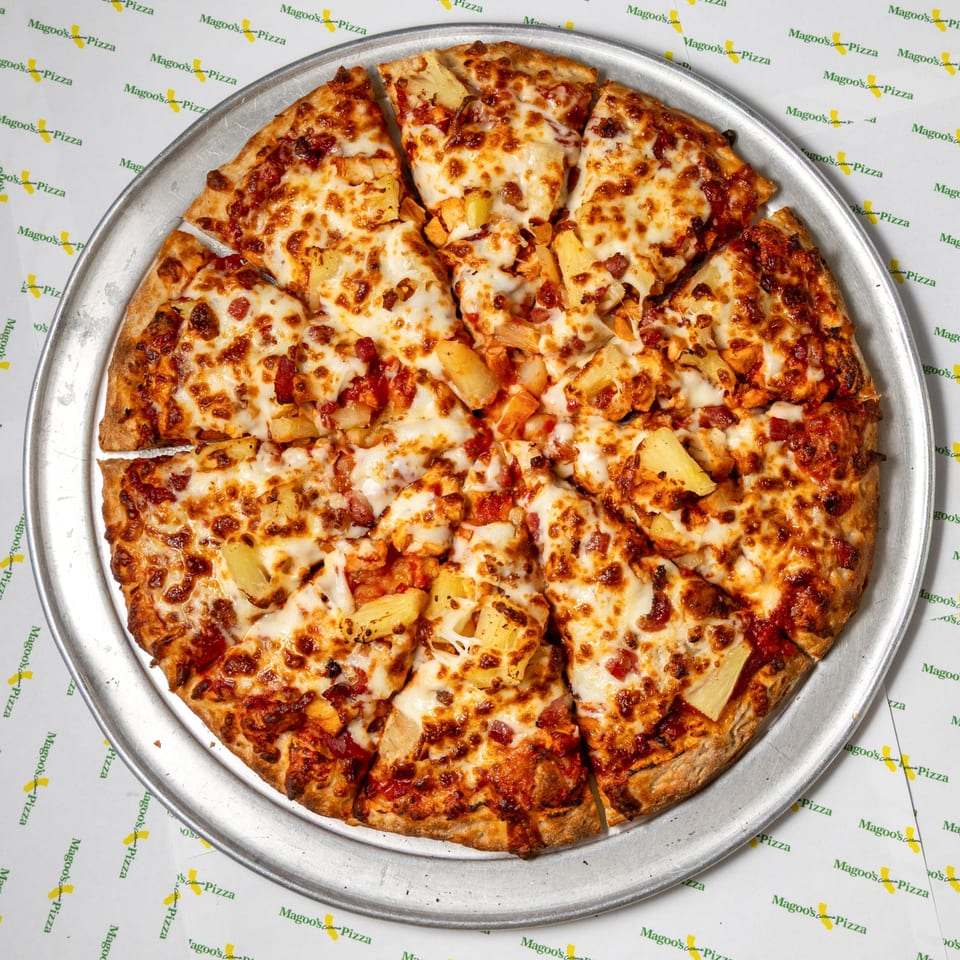 Magoo's California Pizza with pineapple, bacon, and chicken on a metal pizza pan.