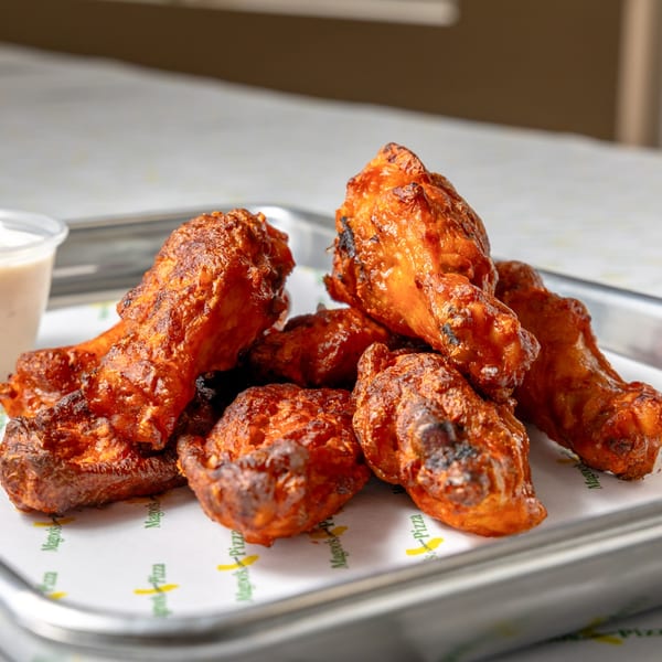 A close-up of Magoo's California Pizza's crispy, saucy chicken wings on a branded paper-lined tray.