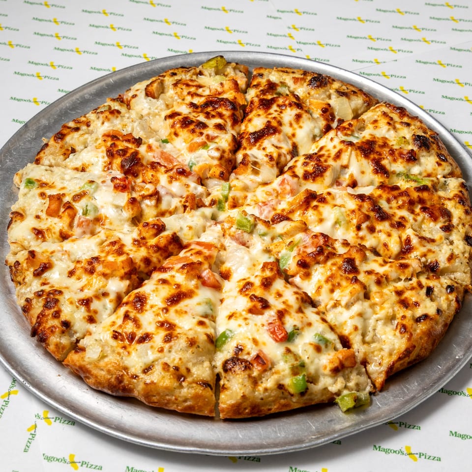 A Magoo's California Pizza, sliced, with melted cheese, chicken, and vegetables on a metal pan.