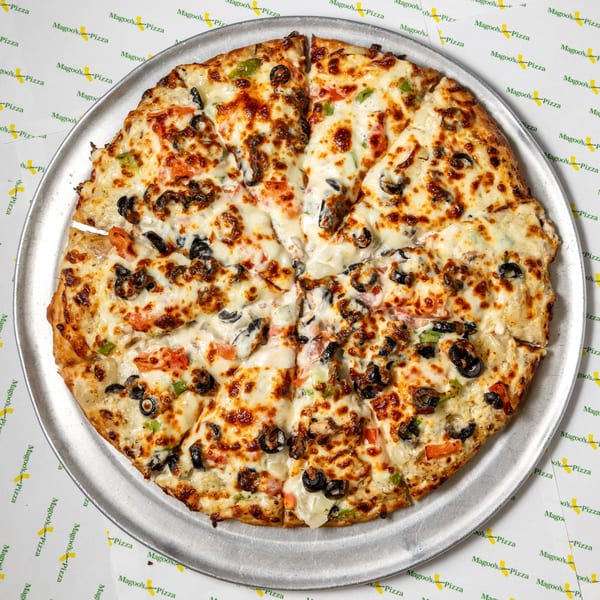 A whole Magoo's California Pizza, sliced, with melted cheese, olives, and vegetables on a metal pan.