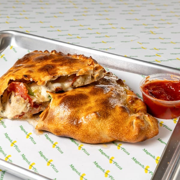 Two golden-brown Magoo's California Pizza calzones, one cut open, with a side of marinara sauce.