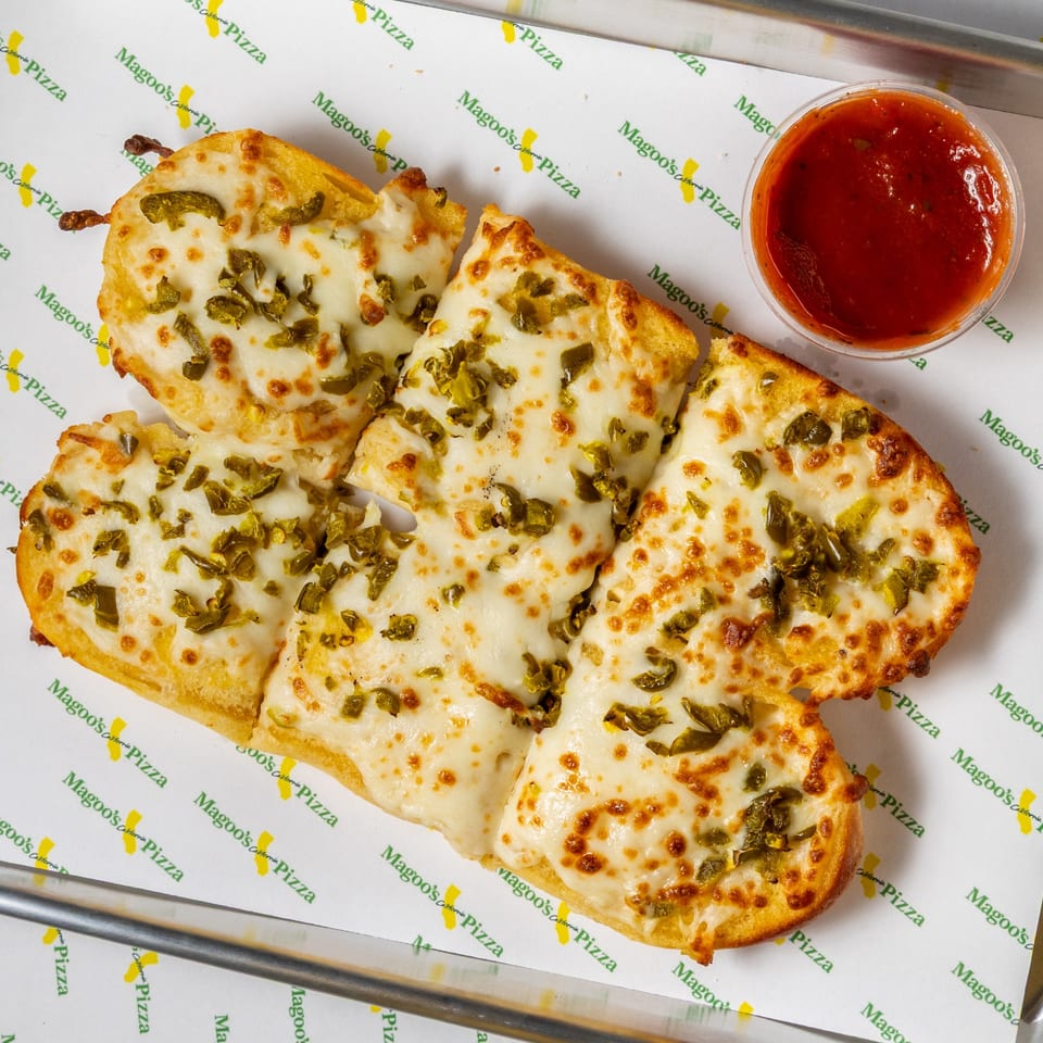 Magoo's California Pizza jalapeño cheese breadsticks with marinara sauce on branded parchment paper.