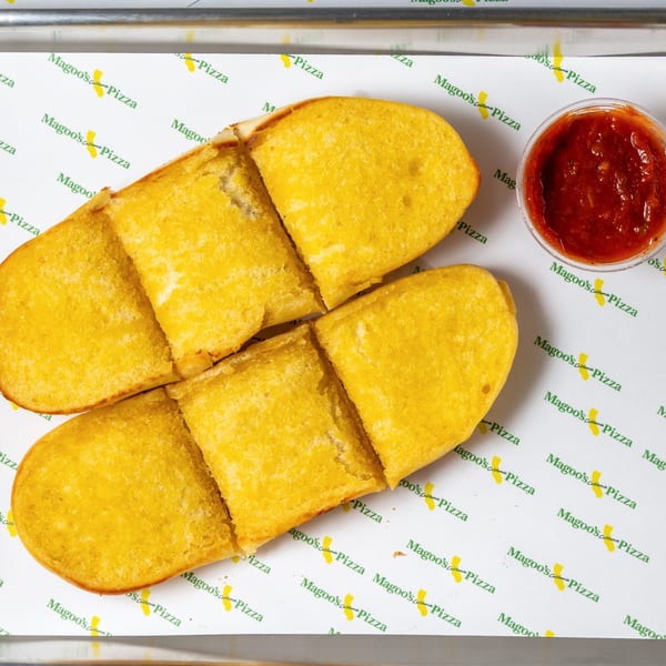 Two golden-brown breadsticks, cut into pieces, with a side of red dipping sauce on Magoo's California Pizza branded paper.