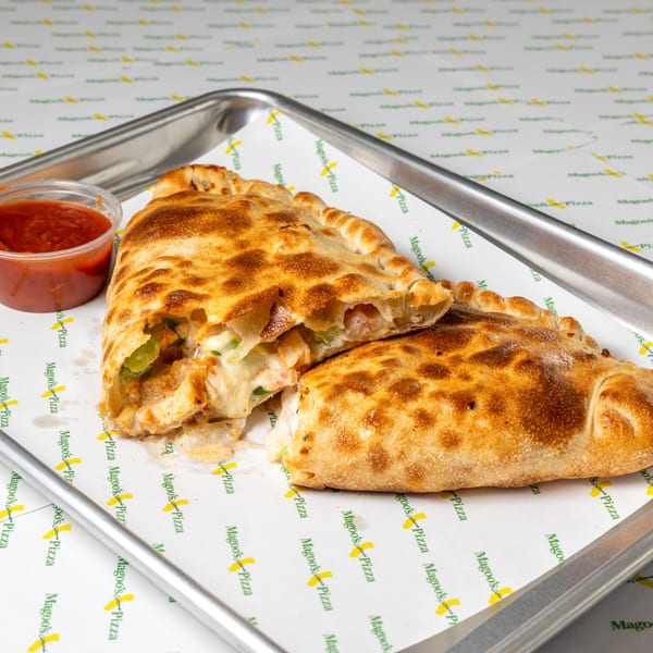 Two golden-brown calzones, one cut open to reveal chicken and cheese, with a side of marinara sauce.