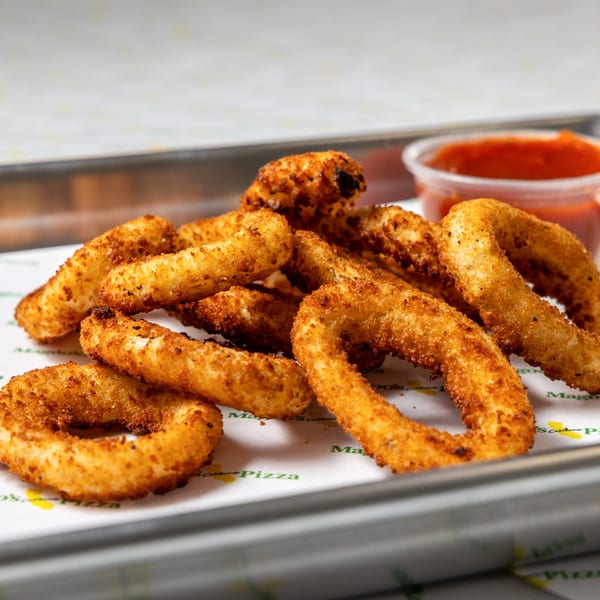 Golden-brown onion rings with a side of red dipping sauce on a metal tray.