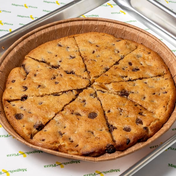 A large chocolate chip cookie, cut into eight slices, in a round brown paper container.